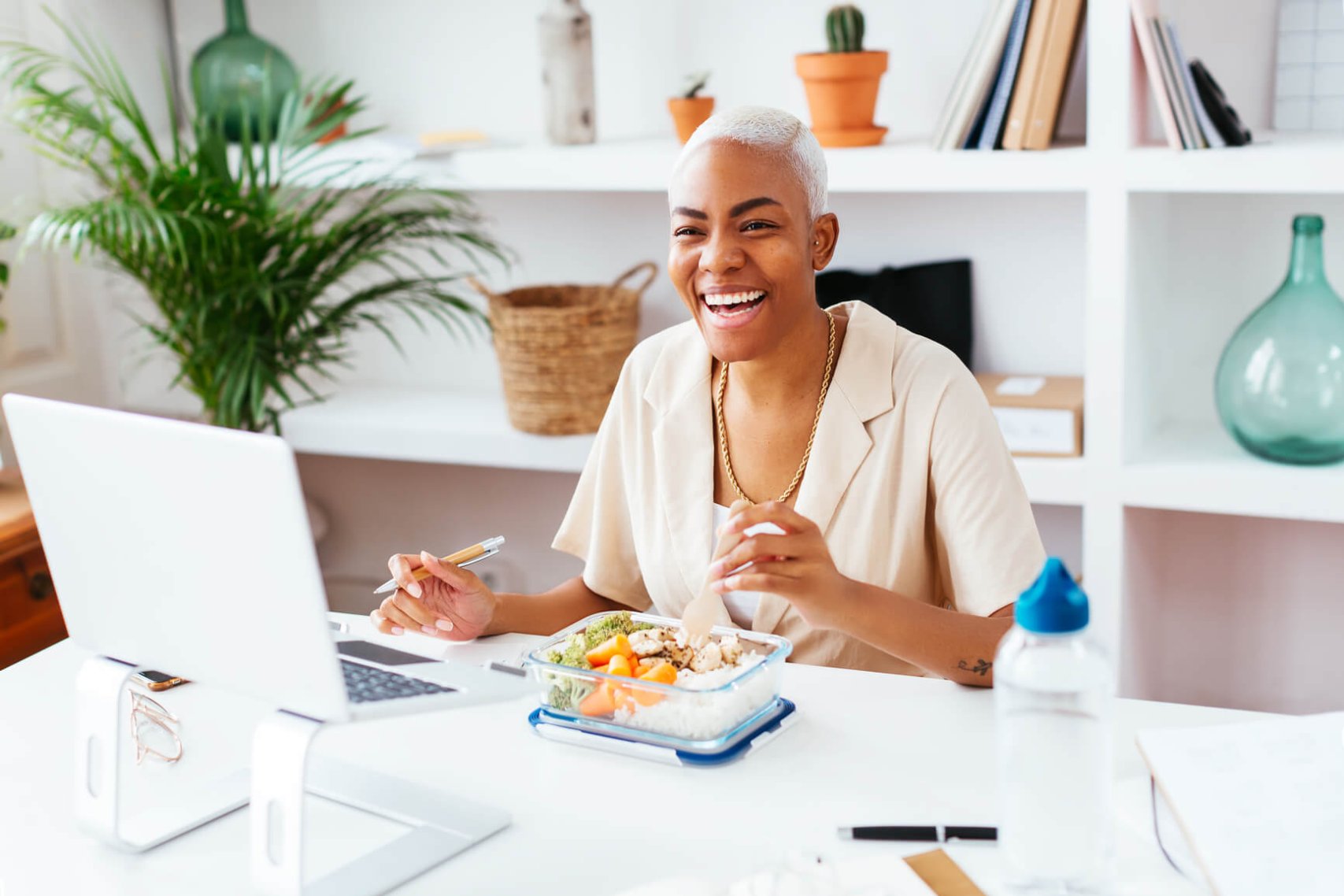 High angle of positive woman with short dyed hair laughing and eating healthy food while sitting at table during lunch in office